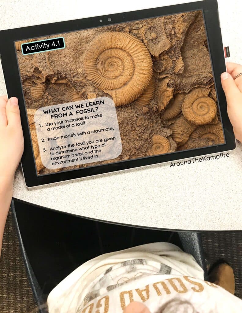 A male third grade student holding an iPad and reading a fossils activity in science class.