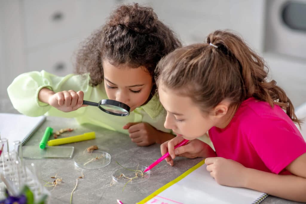 Girls looking through magnifying lenses at school.